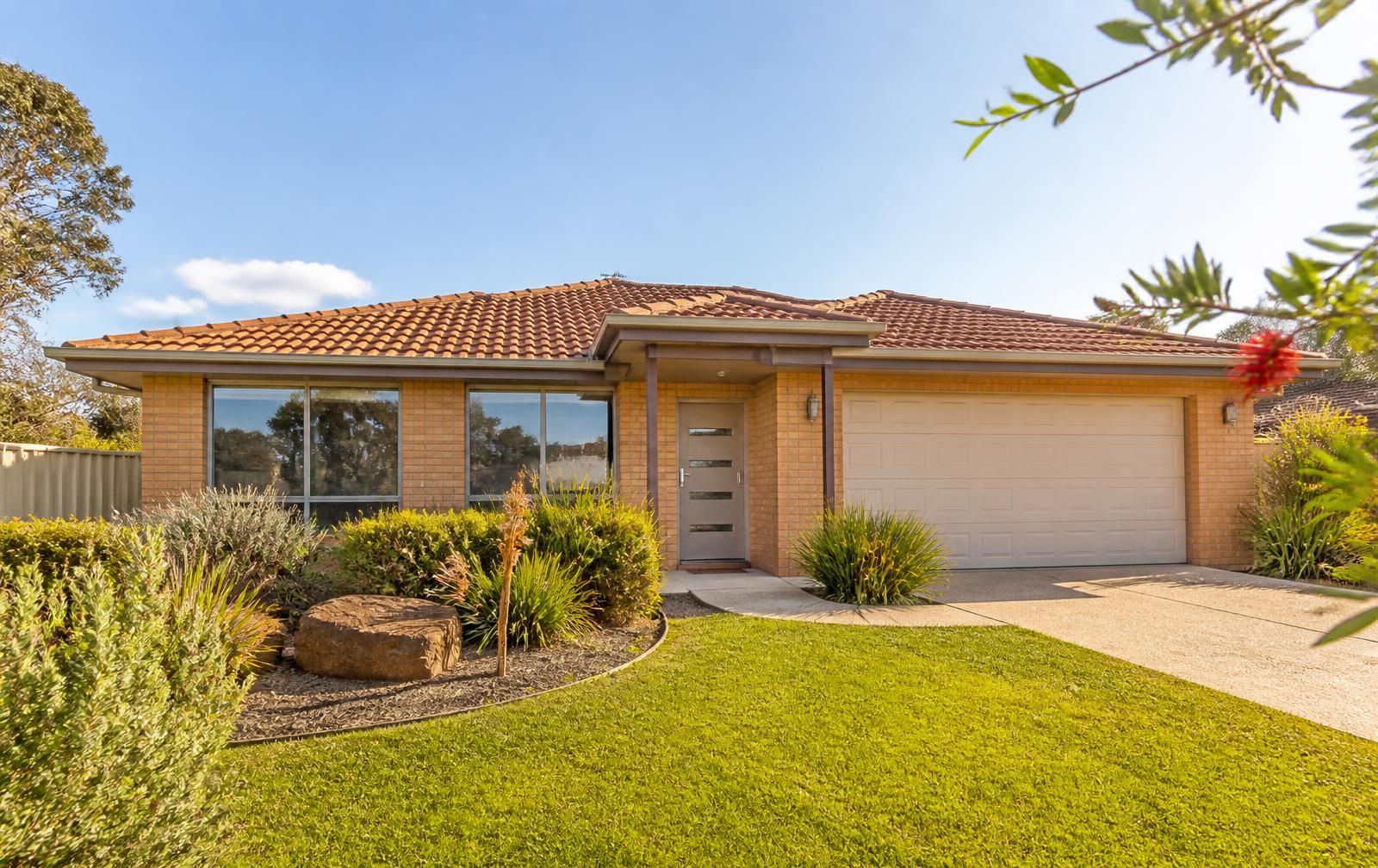 Sunlit Australian brick home with a freshly mown lawn and tidy native garden beds
